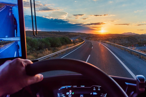 View from the driver's seat of a truck on a highway at dawn with the sun on the horizon.